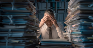 Man with head in hands surrounded by paperwork. The headache that is manual data entry.