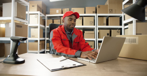 Person sat in stock warehouse with a clipboard and a laptop. Using invoice processing automation,