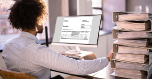 Person using invoice automation software on a computer, pushing pile of paper files away.