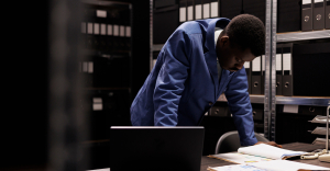 Person manually checking documents, with a laptop by their side. Document fraud detection software would speed up the process.