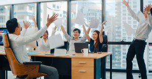 People in an office throwing their hands in the air, with paper flying around - to represent touchless invoice processing.