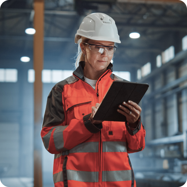Manufacturing process management software shows a person wearing goggles, hard hat, and overalls and using a clipboard.